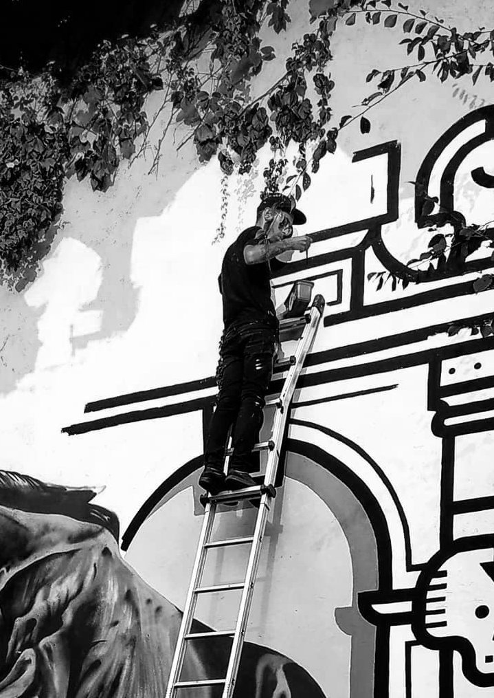 Abel.Bael on a ladder painting a black and white arch mural